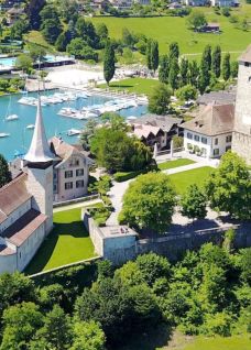 Luftaufnahme der historischen Schlossanlage mit Türmen und Kapelle am türkisfarbenen Thunersee, umgeben von grüner Landschaft und Segelbooten. Ideal für Themen wie Kulturreise, Sehenswürdigkeiten, Mittelalter, Architektur, Tourismus.
©Schloss Spiez csm_schloss-spiez-apero-areal_Zumbrunn-1200_832c37cc67