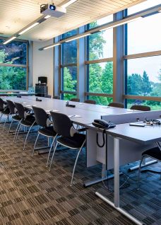 Heller, moderner Seminarraum mit grossen Fensterfronten, Blick ins Grüne und flexibler Tischanordnung für Meetings, Workshops oder Schulungen. Ergonomische Stühle, integrierte Präsentationstechnik und klare Linien schaffen eine professionelle Atmosphäre – ideal für Business-Events am Thunersee im Kanton Bern. ©Seepark Moderner Seminarraum mit Tageslicht