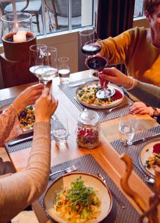 Vier Personen stossen am liebevoll gedeckten Tisch mit Wein an; serviert werden Pasta und frischer Salat in warmer, einladender Atmosphäre. Ideal als Rahmen für ein entspanntes Firmenevent, Networking oder Incentive am Thunersee – kulinarisch, persönlich und geschäftlich inspirierend. Teamdinner mit Seeblick