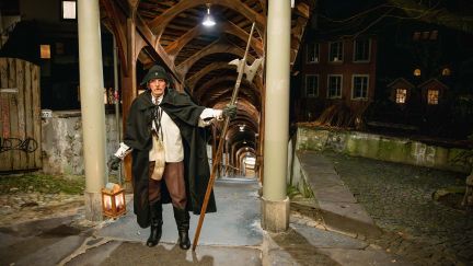 Traditioneller Nachtwächter führt durch den beleuchteten Laubengang in Thun – stimmungsvolle Abendatmosphäre für Rahmenprogramme und Gruppen. ©Thun-Thunersee Tourismus Nachtwächter im historischen Laubengang in Thun mit Laterne und Hellebarde