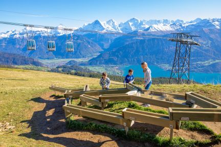 Holz-Kugelbahn auf einer Sonnenterrasse, daneben Gondelbahn und Panorama über den Thunersee – ideal für Pausen und Gruppenmomente in der Region. ©Niederhorn Kugelbahn-Spielplatz mit Blick auf den Thunersee und die Alpen